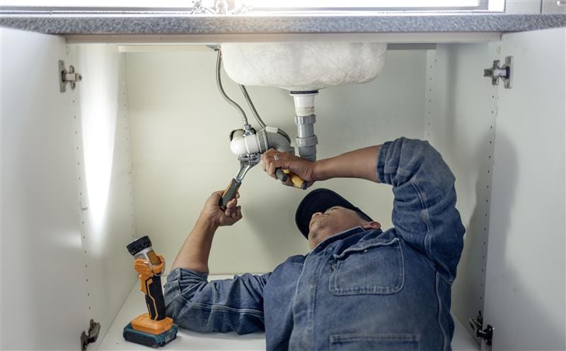 Plumber repairing pipes beneath a bathroom sink in Spring Valley