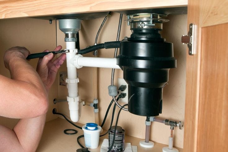 Plumber installing a garbage disposal beneath a kitchen sink in Spring Valley