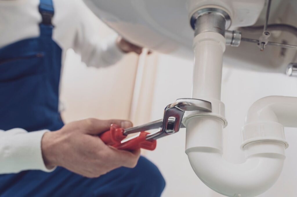 Plumber repairing a white drain pipe beneath a sink in Spring Valley