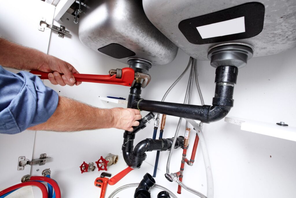 Plumber repairing drain pipes beneath a kitchen sink in Spring Valley